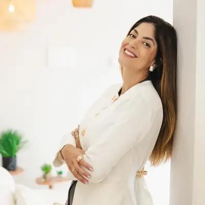 Dra. Thamara Martins sorrindo de jaleco branco, encostada na parede da clínica